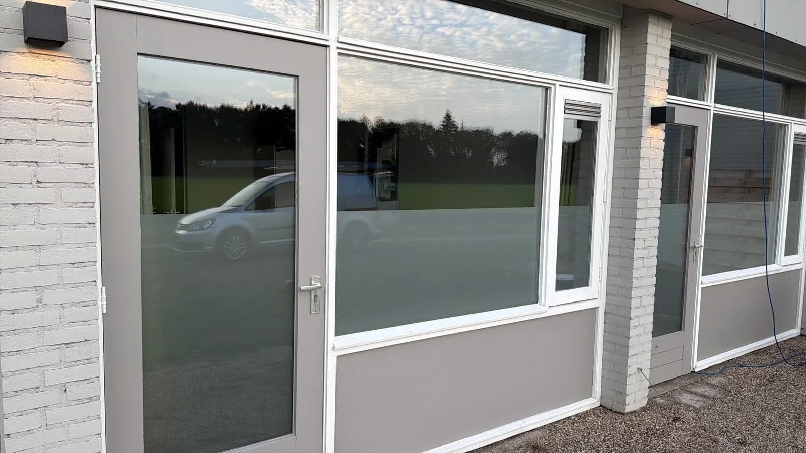 Schone deur en raampartij van een bedrijfspand, waarin de lucht spiegelt