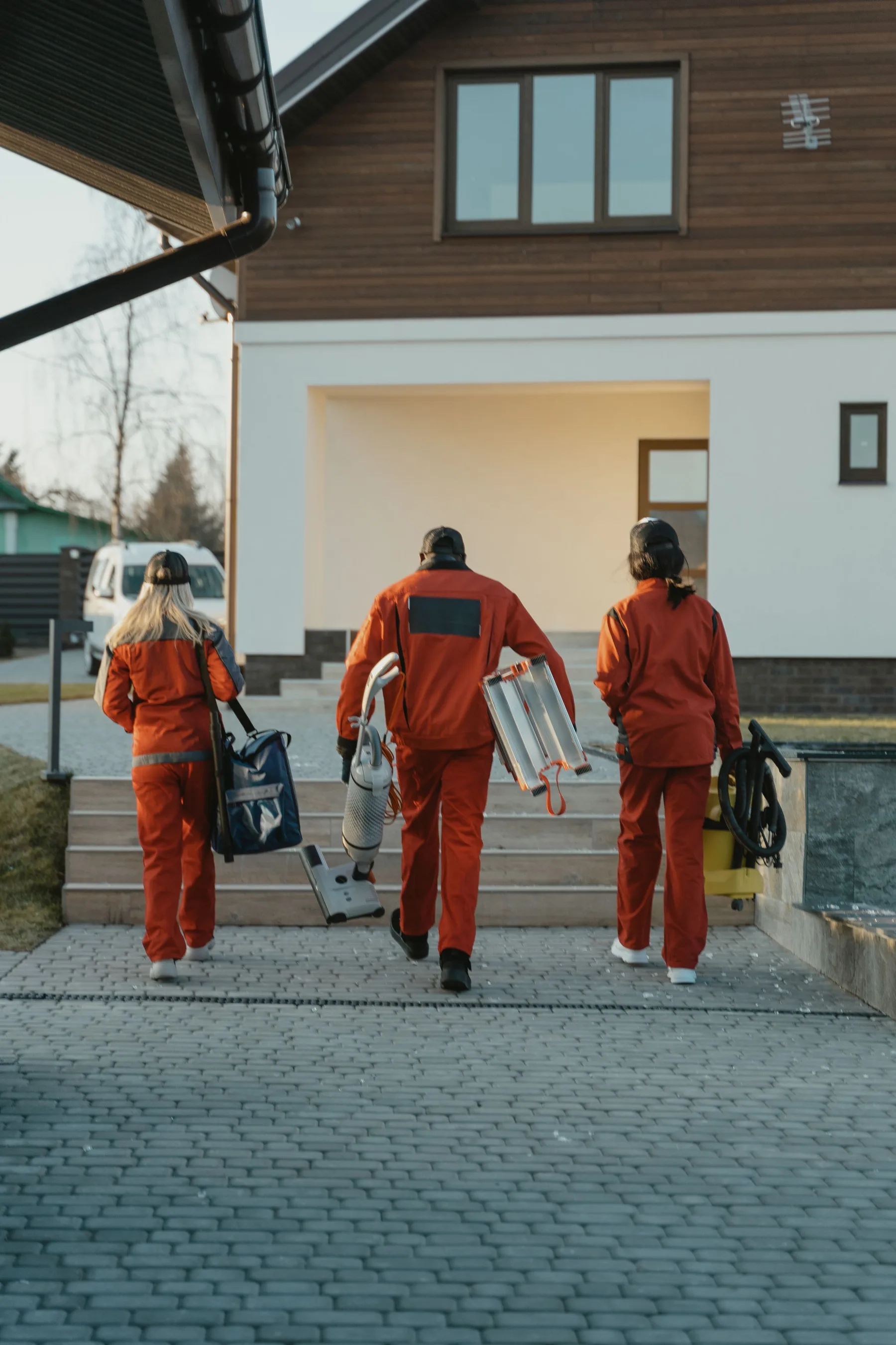 Drie schoonmakers lopen met stofzuigers en een trap naar een nieuwe woning